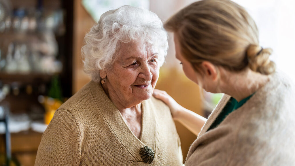 Pflegekraft spricht einfühlsam mit älterer Frau – emotionale Betreuung im Alter.