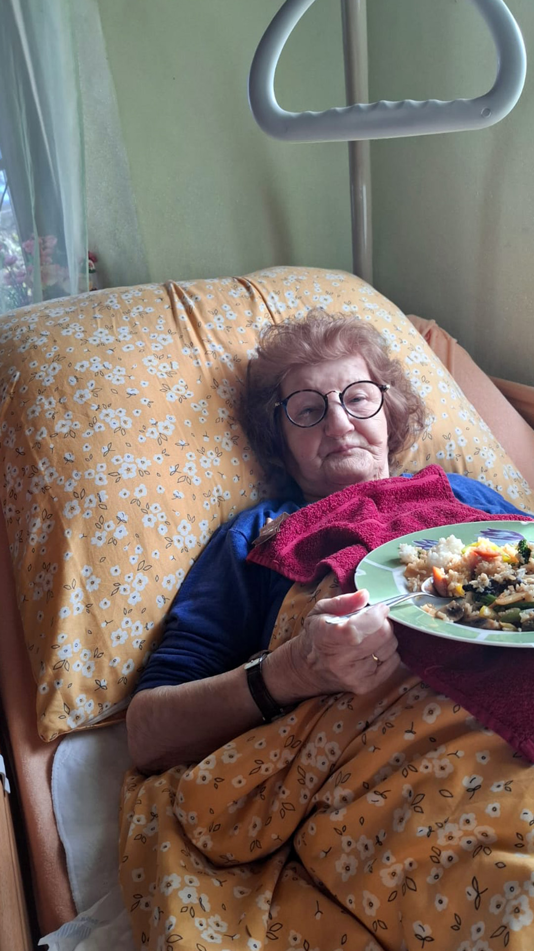 Über uns 13 Ältere Frau genießt im Bett ein frisch zubereitetes Essen, das ihr von der Pflegerin gebracht wurde.